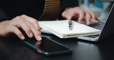 Geschäftsmann berührt mobile Smartphone digitale Internet-Technologie-Netzwerk mit Computer Laptop und Stift Buch auf dem Schreibtisch.